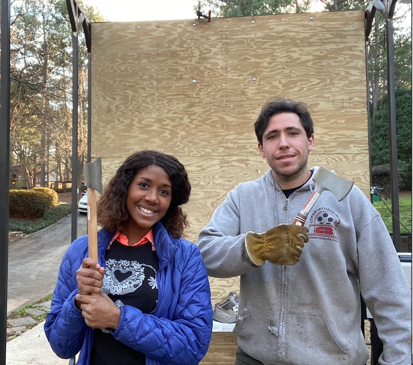 Eden and Adam holding axes in front of their ax throwing trailer.