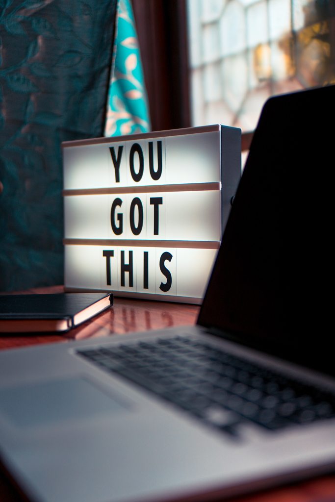 A close up of a desk, with laptop and book, plus a lit block with the words "You Got This" in big letters.